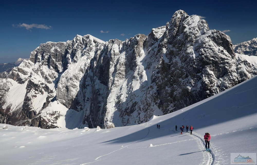 Traverz směrem ke Kotovu sedlu se skalnatým hřebenem Šite v pozadí. Skialpinistická túra nad Kotovo sedlo pod severními srázy Jalovce v Julských Alpách.