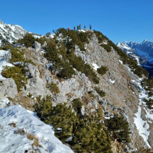 Skialpinisti na vrcholu Srednji vrh při pohledu od výhlídkové lavičky