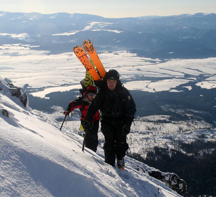 Široké lyže připevněné v čele batohu vedle sebe - obdobné připevnění snowboardu